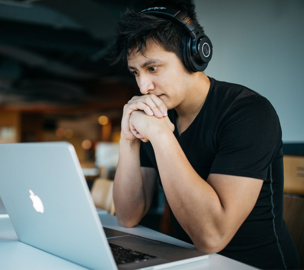 Photo d'un jeune homme équipé d'un casque audio et qui regarde avec attention l'écran d'un ordinateur portable